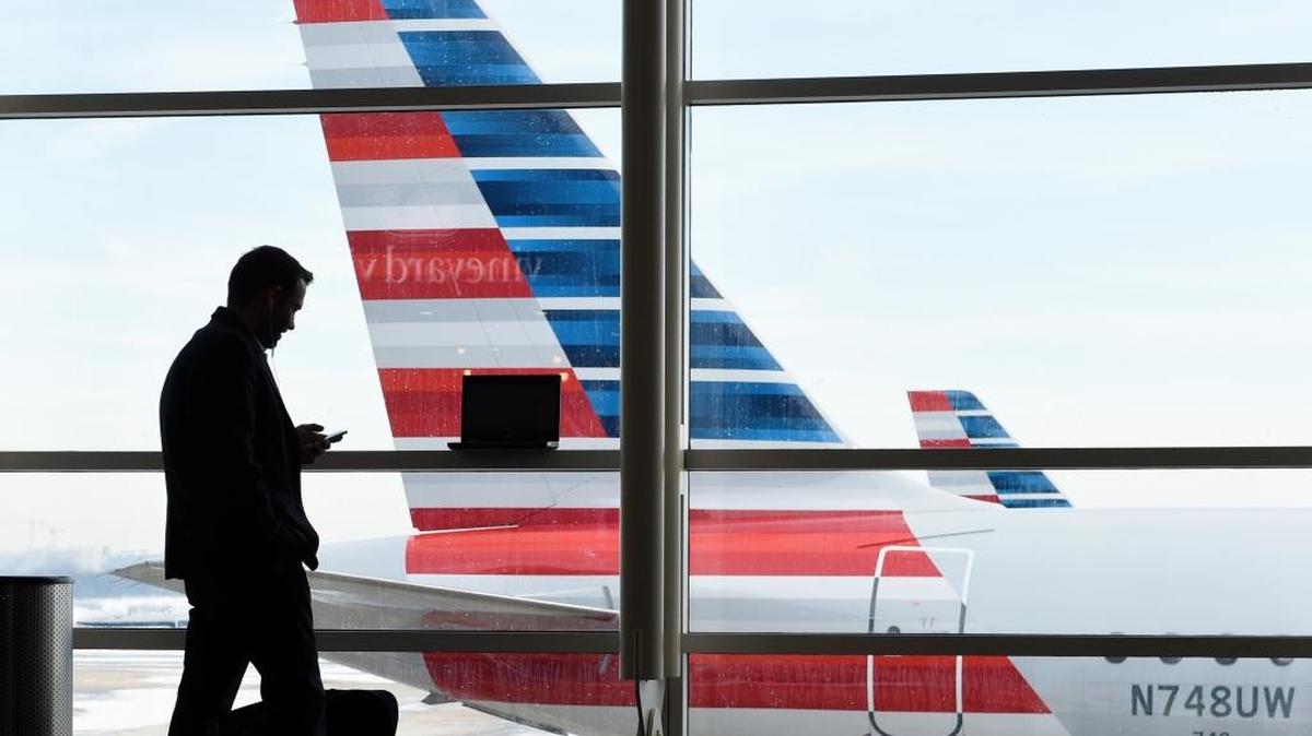 In this Jan. 25, 2016, file photo, a passenger talks on the phone as American Airlines jets sit parked at their gates at Washington's Ronald Reagan National Airport. After 15 years of cutbacks, U.S. airlines are starting to add back some small perks for everyday coach passengers.