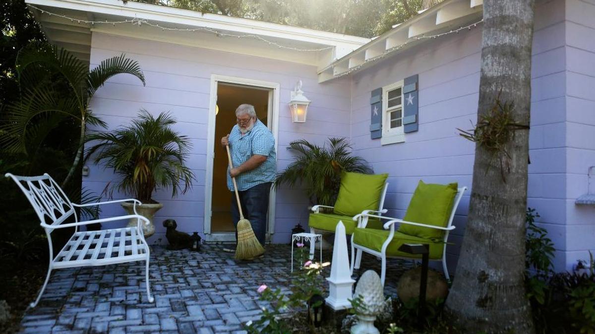 In this Nov. 21, 2016 photo, Randall Baker, a College Park landscape architect who rents out two cottages next door to his home as Airbnb rentals, sweeps the front patio of one of his rentals, in Orlando, Florida. The city says Baker is violating zoning rules, but he argues he is being singled out. Similar debates are playing out across the state.