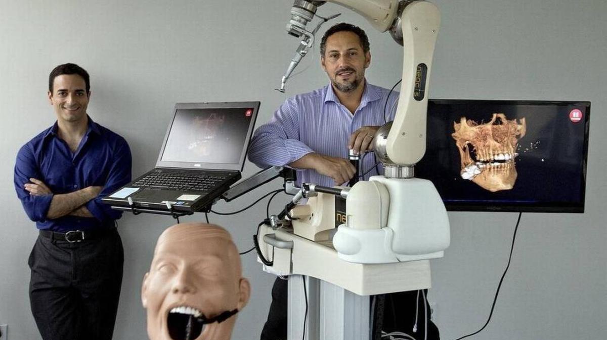 Alon Mozes, left, and Juan Salcedo started the healthcare robotics company Neocis. They are shown with an early version of Neocis’ robotic guidance system for the fast-growing dental implant market, which received FDA clearance and is now being marketed. Both co-founders worked together at Mako Surgical before founding Neocis.
