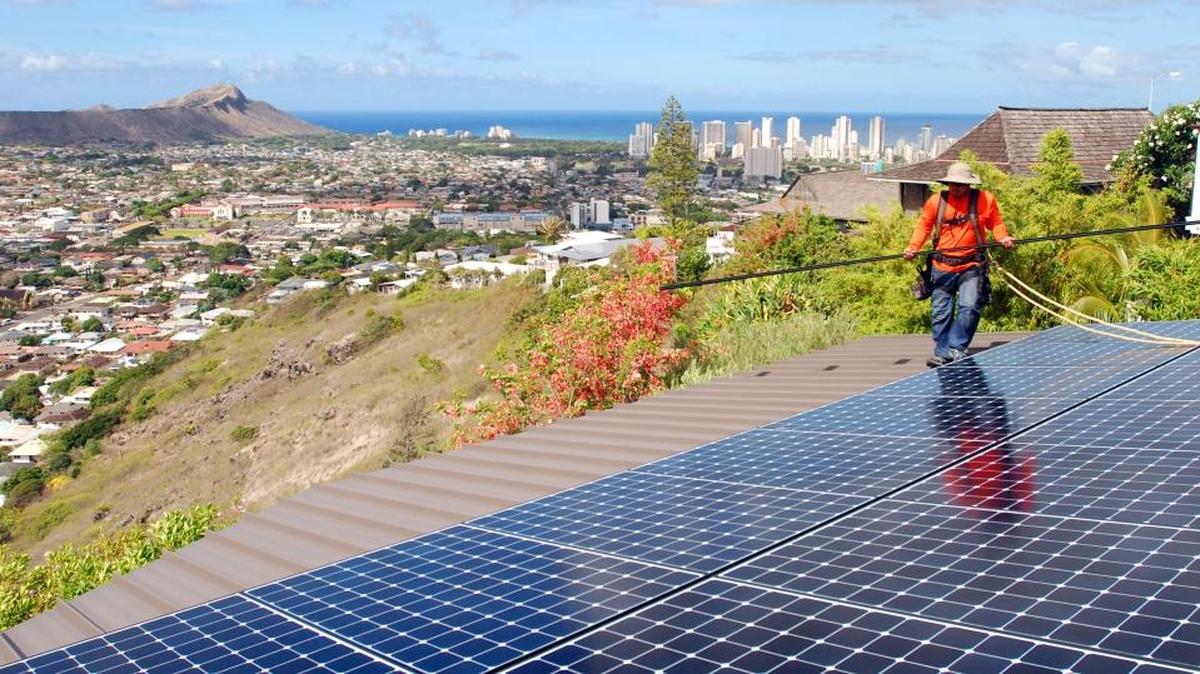 Radford Takashima, installer for RevoluSun, works on a solar panel installation on a roof in Honolulu. Hawaii is a national leader in rooftop solar power, and the state has an ambitious goal of using only renewable energy by 2045. A proposal by NextEra of Juno Beach, Florida, to buy out Hawaii Electric Industries was not approved by state regulators.