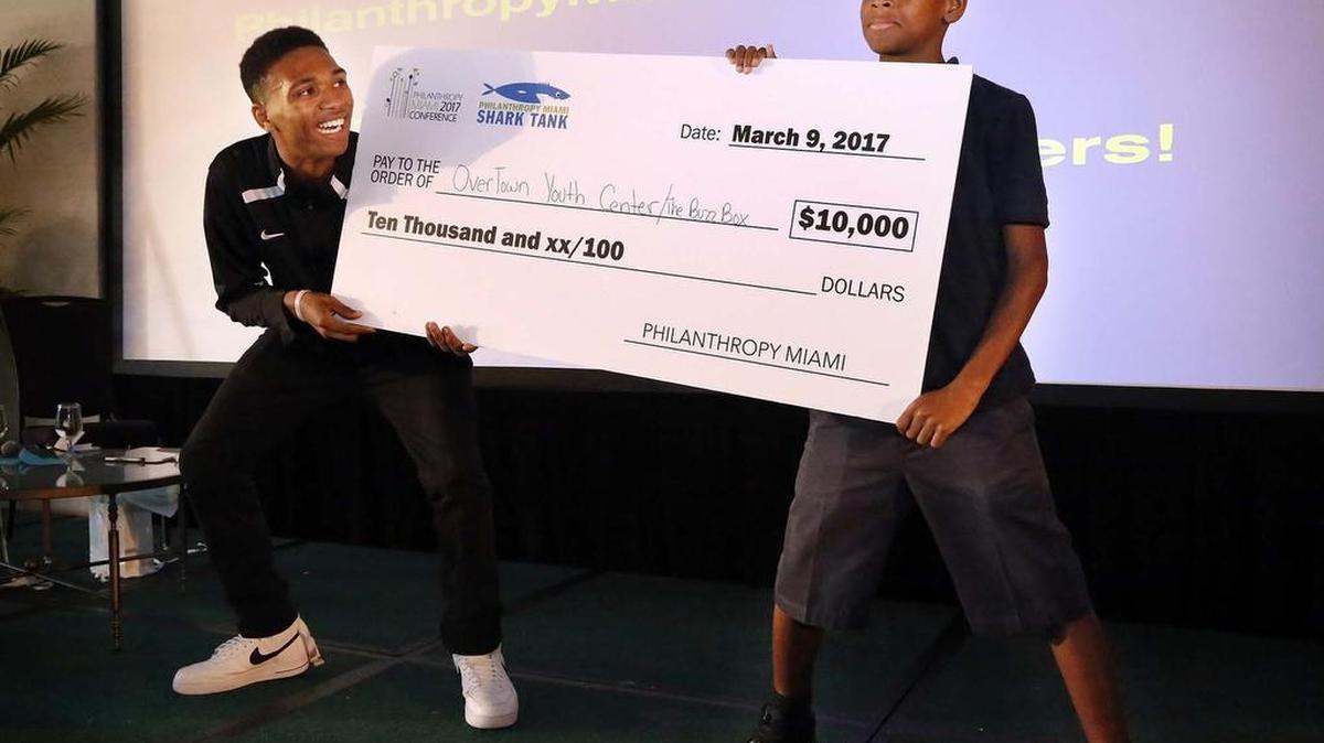 Clifton Ross, left, and Lavaris Stanford hold a check for $10,000 that was presented Thursday to Overtown Youth Center’s Buzzbox, which builds and runs pop-up barbershops made out of shipping containers.