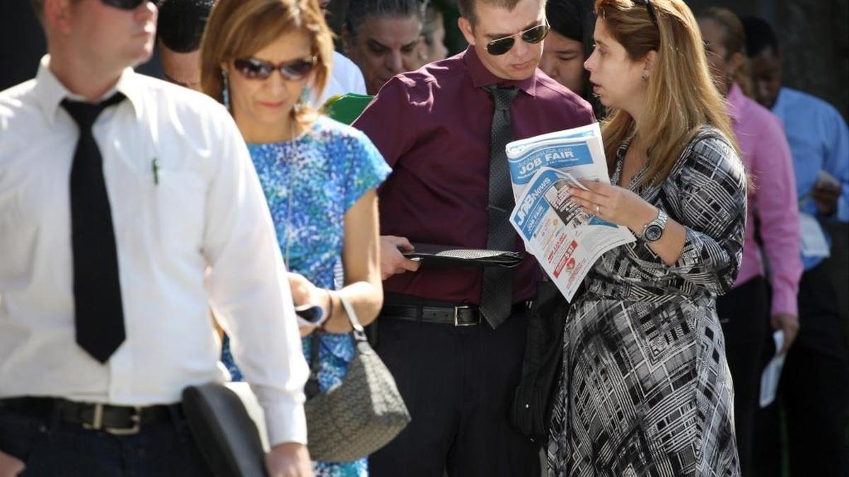 
Job seeker Youssef Caraballo, 37, third from the left, and wife, Maylyn Caraballo, 37, look through the job fair program as they line-up outside the Shula Hotel & Golf Resort for a job fair in Miami Lakes in April.
