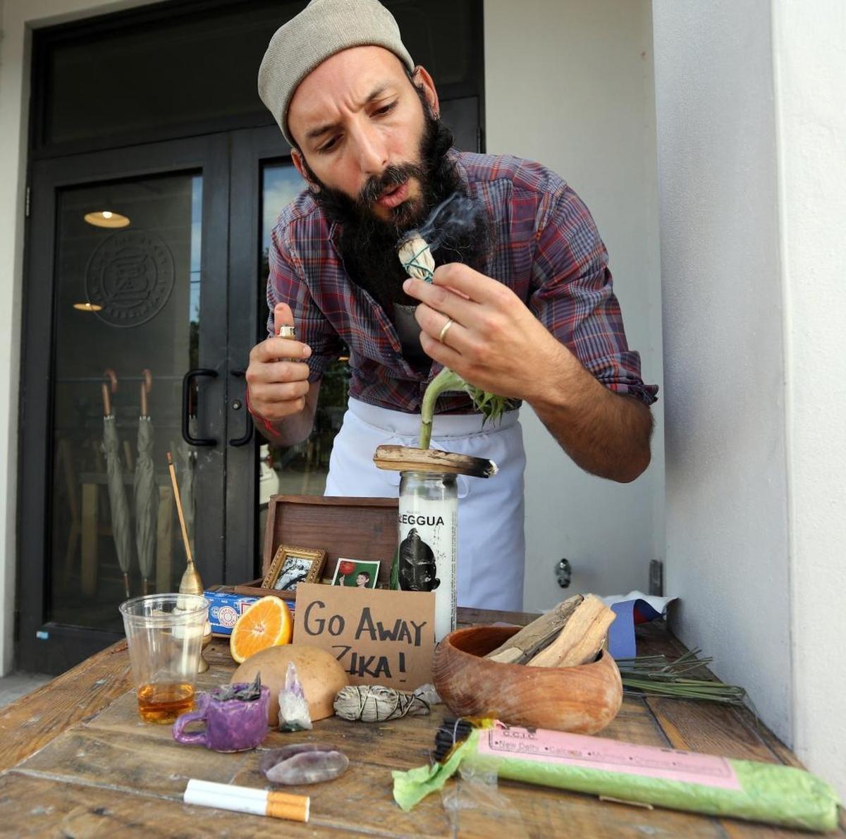 Wynwood’s, Zak the Baker, (Zak Stern) lights a stick of dried sage to add to his “Go Away Zika” shrine outside of his popular Wynwood bakery in August. Zak is trying to make light of of the Zika outbreak that has affected his walk-in store’s daily business.