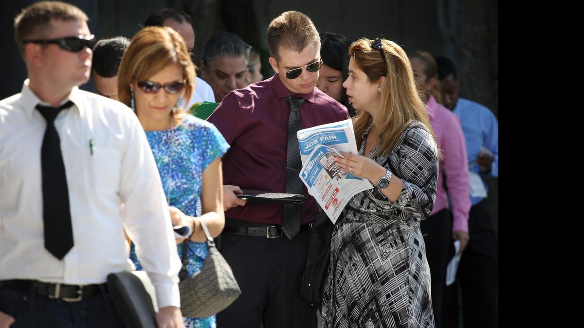 
Job seeker Youssef Caraballo, 37, third from the left, and wife, Maylyn Caraballo, 37, look through the job fair program as they line-up outside the Shula Hotel & Golf Resort for a job fair in Miami Lakes on April 15.
