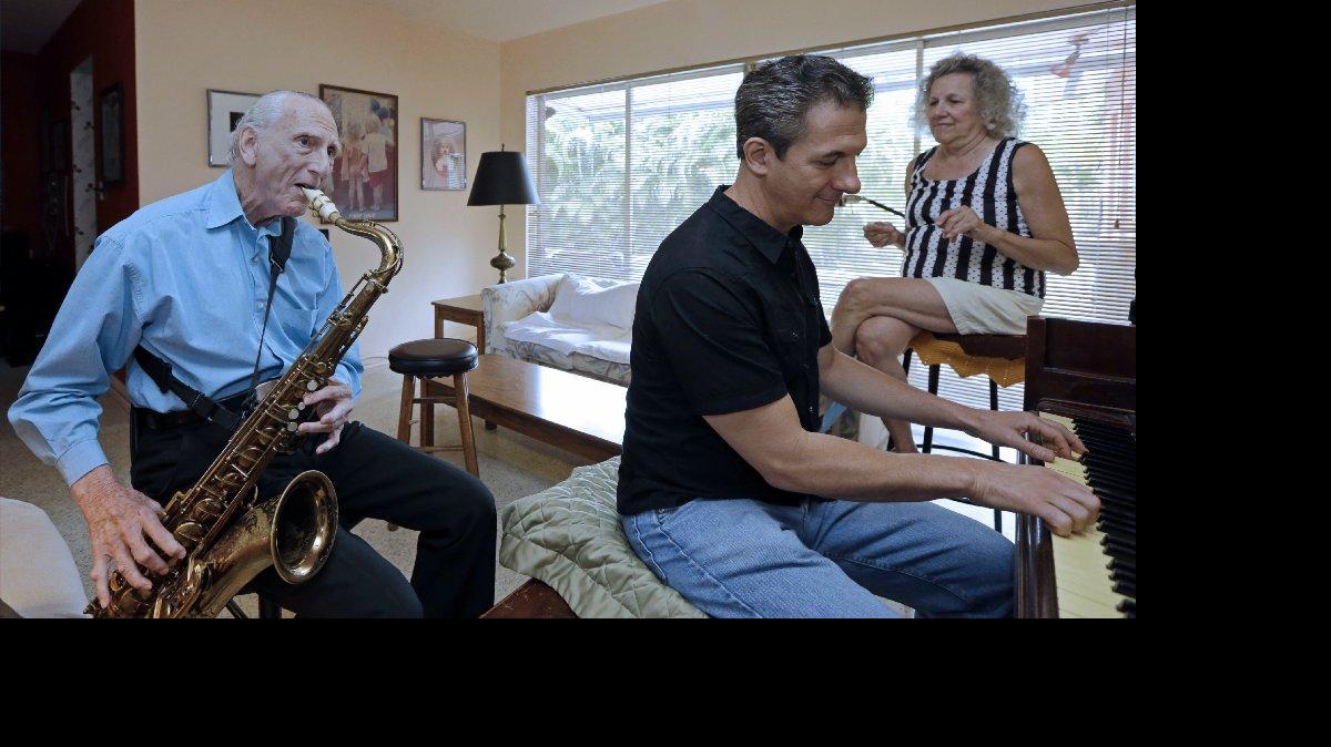 
In this May 11, 2015 photo, Al Karp, left, plays the saxophone as he rehearses with his son Larry, center, and wife Saundra, right, at their home in North Miami Beach, Fla. The trio performs old standards locally as the Karp Family to ease stress and help raise money to save their home from foreclosure. (AP Photo/Alan Diaz) 
