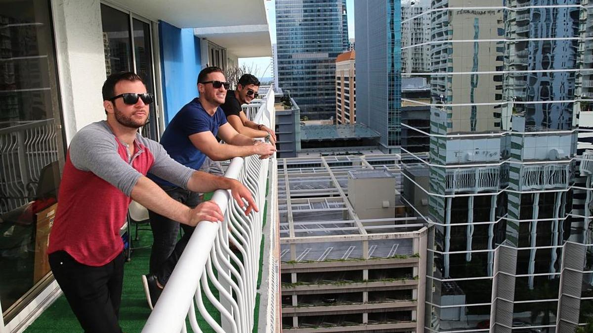 (l. to r.) Roommates Alex Needelman, Aaron Feuer and Devin Healy enjoy the view from the balcony of the apartment they share at the Club at Brickell Bay in Miami.