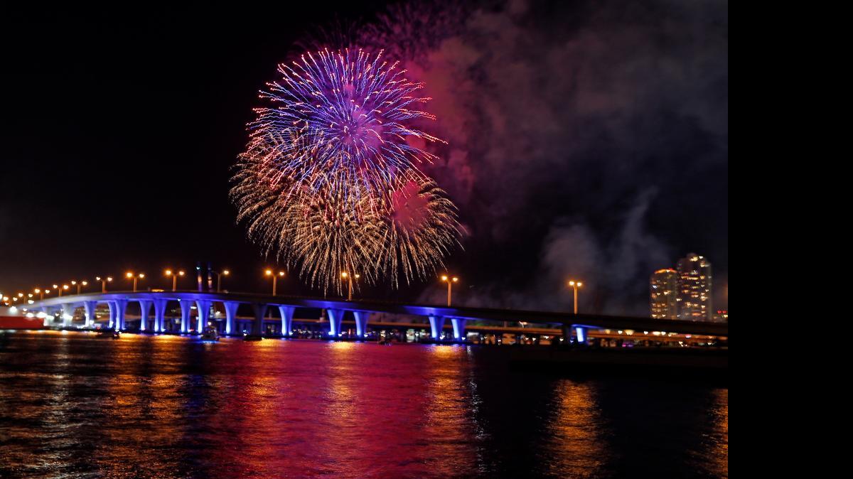 
Fourth of July fireworks displays are scheduled throughout the region on Saturday. In this photo from last year, pyrotechnics are seen over the bridge leading to the Port of Miami as people watch from the Museum Park in Miami.
