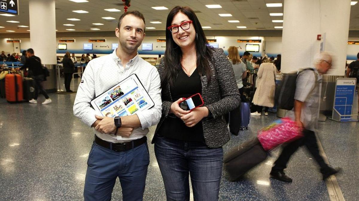 Caribu CTO Alvaro Sabido and CEO Maxeme Tuchman display their tech startup on an iPad and an iPhone at Miami International Airport as travelers move past on Thursday. Sabido and Tuchman say that Caribu is the type of app that people easily can use at airports to read to their kids. It offers a library of more than 200 books for children ages 3 to 7.
