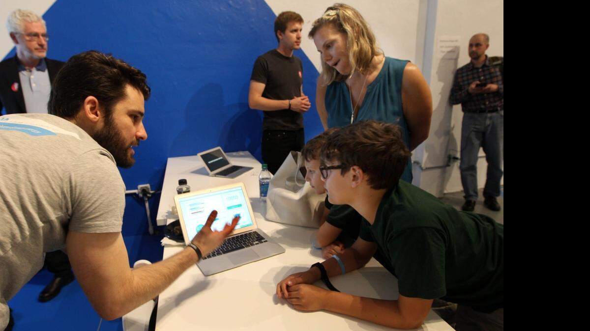 
Curtis Tonge explains to Jed Hoffman, (center) and his brother Isaac Hoffma, (right) and mother Joana Hoffman, (back) about energy managment at Smart City Startups, which had about 100 startups demoing their products, all products that help cities work beter. This took place at the Wynwood Warehouse Project.

