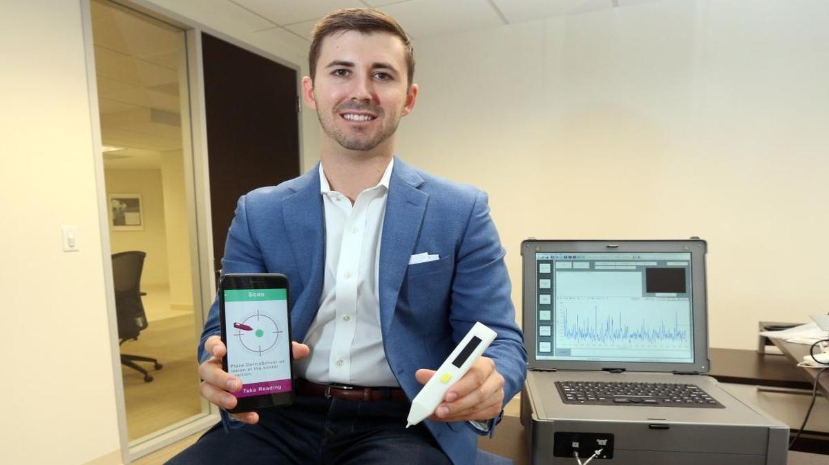 Cody Simmons is CEO of DermaSensor, a Miami-based health-tech startup that is developing a medical device that aims to detect the risk of skin cancer. A user would scan a mole or lesion with the device and the technology inside the device would determine whether the lesion is potentially cancerous, based on its data and algorithm. A prototype of the handheld device that Simmons is holding is a little larger than a pen, but the device started out at as a 30-pound desktop machine that sits next to him. The technology has been miniaturized to be contained in a hand-held device.