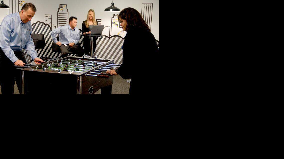 
e-Builder President and CEO Ron Antevy, left, and recently hired employee Lisa Ruggieri, right, play foosball in the game room of the company office in Plantation.
