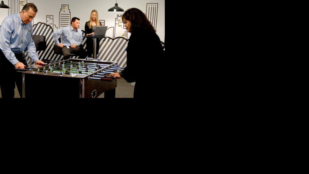 
e-Builder President and CEO Ron Antevy, left, and recently hired employee Lisa Ruggieri, right, play foosball in the game room of the company office in Plantation.

