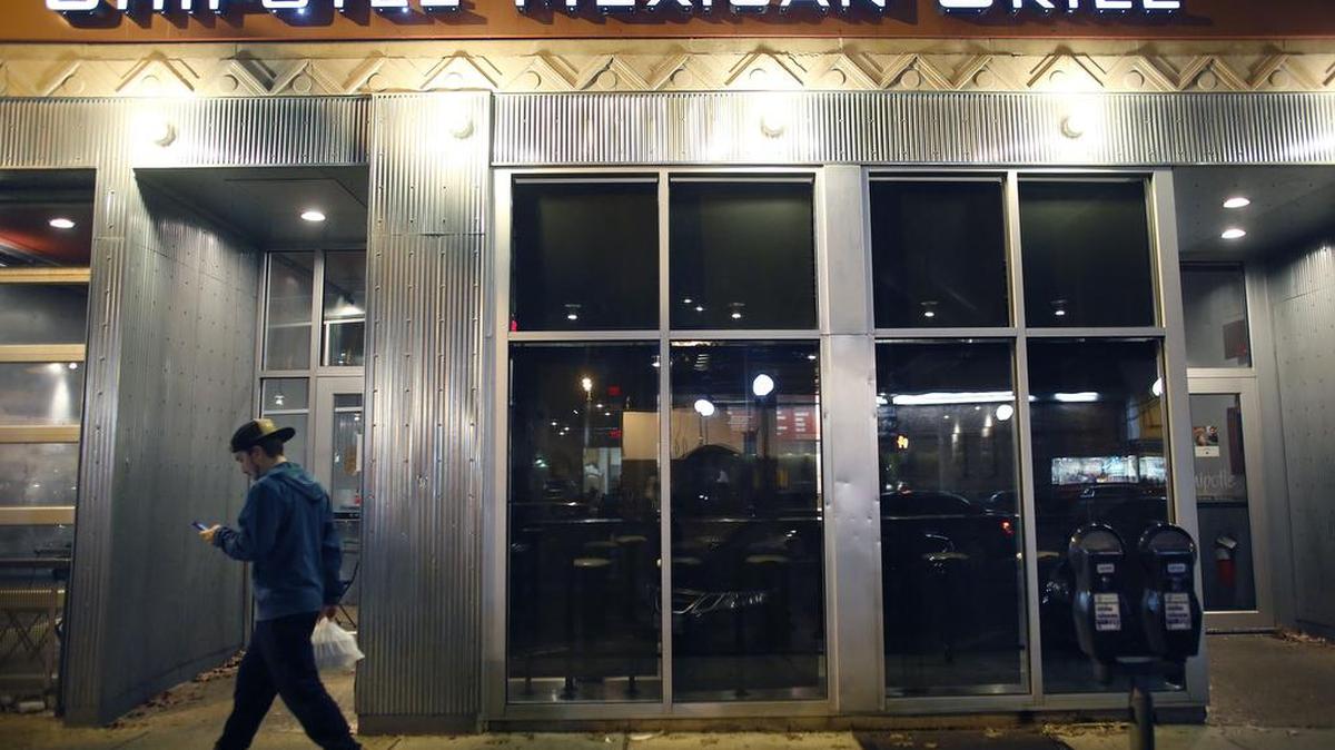 A man walks near a closed Chipotle restaurant in the Cleveland Circle neighborhood of Boston on Monday, Dec. 7, 2015.