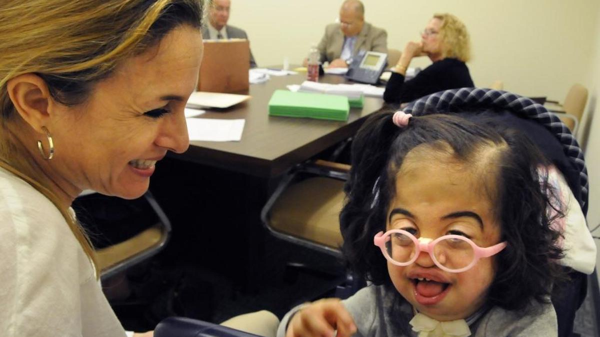 The mother, left, cares for her disabled child, right, during a hearing in 2012 in which her mom is suing the state to get more in-home nursing care. The hearing was before a state administrative judge via telephone.