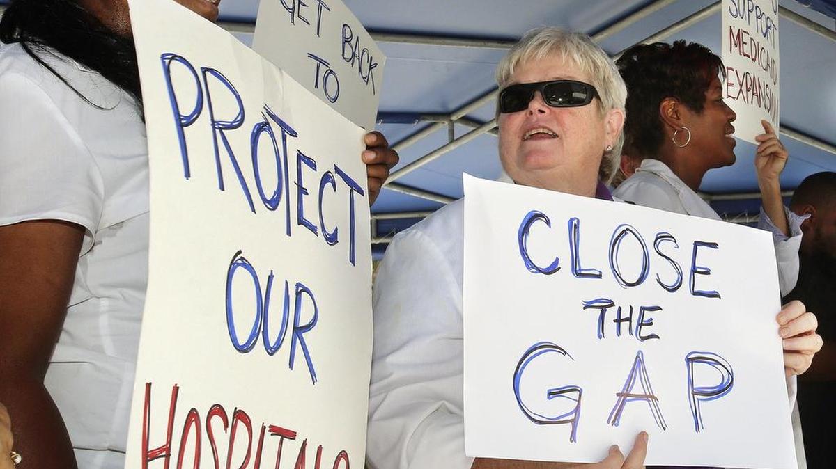 Registered nurses Lisa Ward, left, and Barbara Scollon, center, hold signs at a rally in support of Medicaid expansion in Florida held at Miami’s Jackson Memorial Hospital in May 2015. Six years later, the Florida Legislature still won’t expand the program.
