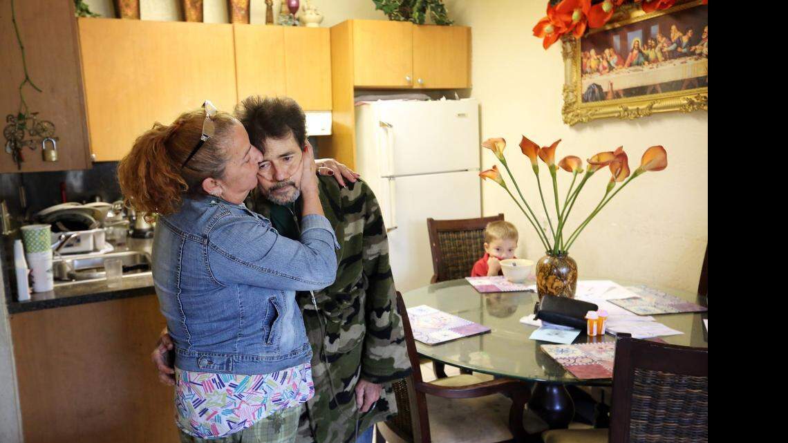 
Paula Bazain, 55, comforts her ill husband, Martin Bazain, 58, in the kitchen of their Miami apartment as their grandson, Giovanny, 5, eats lunch at the table.
