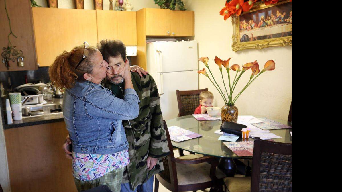 
Paula Bazain, 55, comforts her ill husband, Martin Bazain, 58, in the kitchen of their Miami apartment as their grandson, Giovanny, 5, eats lunch at the table.
