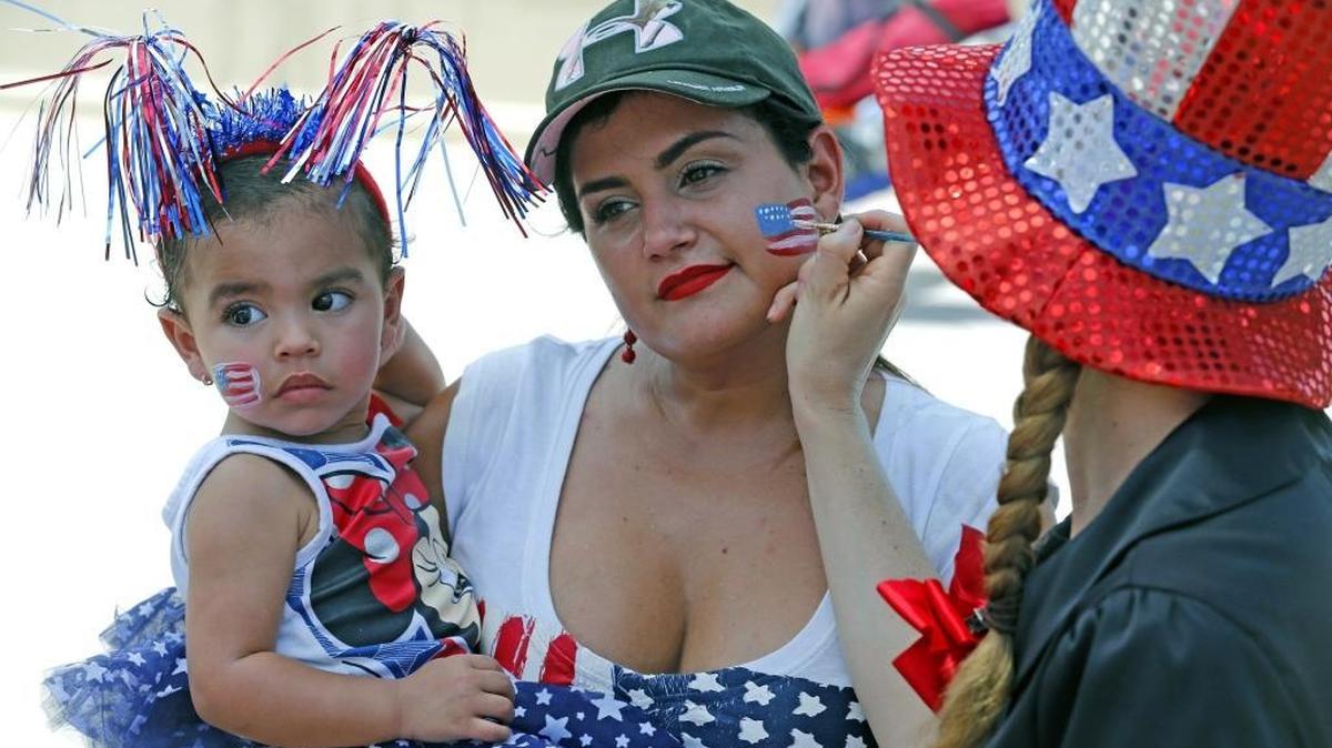 Marcela Alzate, holding her daughter Olivia 1, gets a flag painted on her face as she celebrates July 4 in North Beach in 2016.