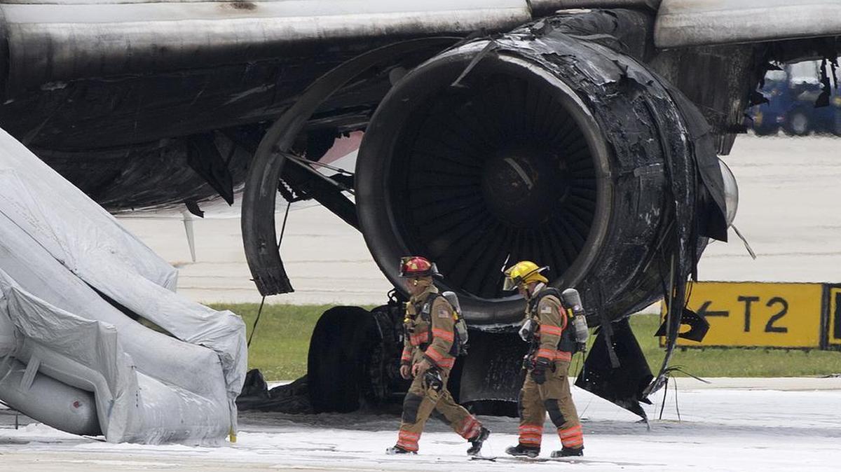 Firefighters walk past a burned engine of an airplane, Thursday, Oct. 29, 2015, at Fort Lauderdale/Hollywood International Airport in Dania Beach, Fla. The passenger plane's engine caught fire Thursday as it prepared for takeoff, and passengers had to quickly evacuate on the runway using emergency slides, officials said. The Dynamic Airways flight was headed to Caracas, Venezuela.