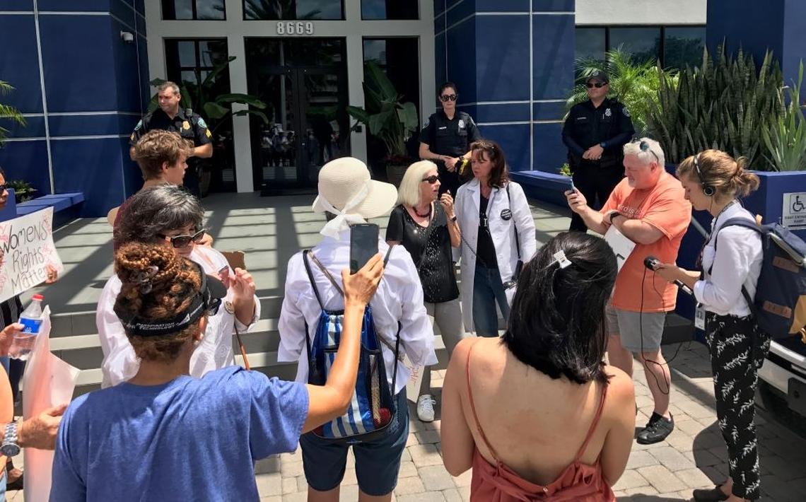 Protesters gather in front of Sen. Marco Rubio’s Doral office on Tuesday to voice their concerns about the future of healthcare, while three police officers stand at the top of the stairs.