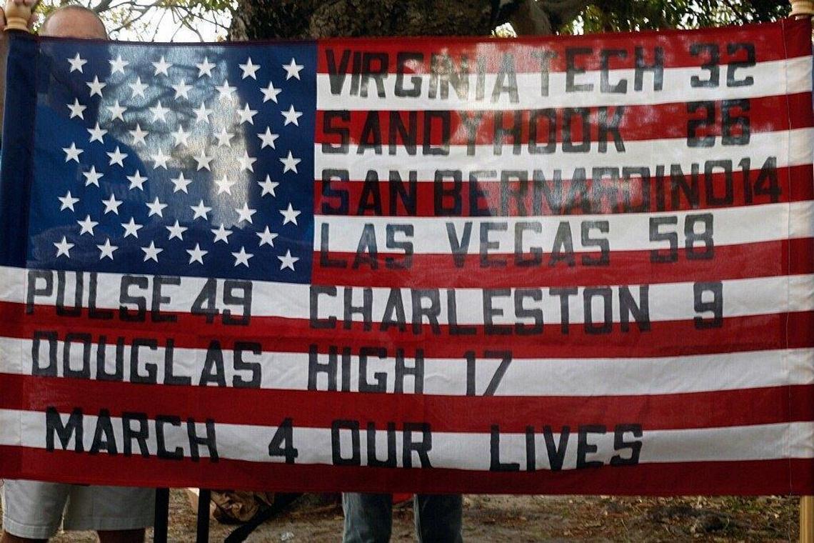 An American flag with a list of the most recent mass shooting in the country is shown holds a T-shirt before the Miami Beach March for Our lives rally on Saturday.