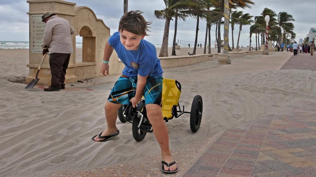 Anthony Tasse, center, struggles to get his three-wheel cycle out of sand that blew on Hollywood Beach’s broadwalk on Sunday, Dec. 20, 2015.