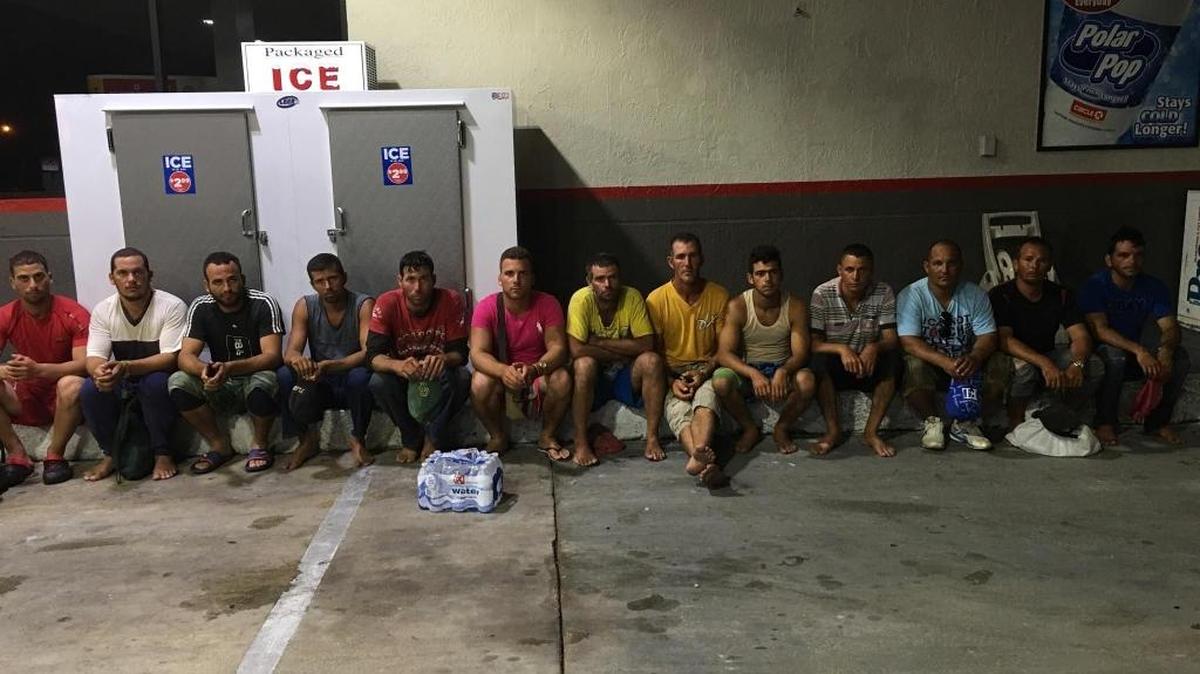 Thirteen Cuban men sit on the curb of a Key Largo gas station after arriving from what they said was a four-day sea journey from their homeland to the United States.