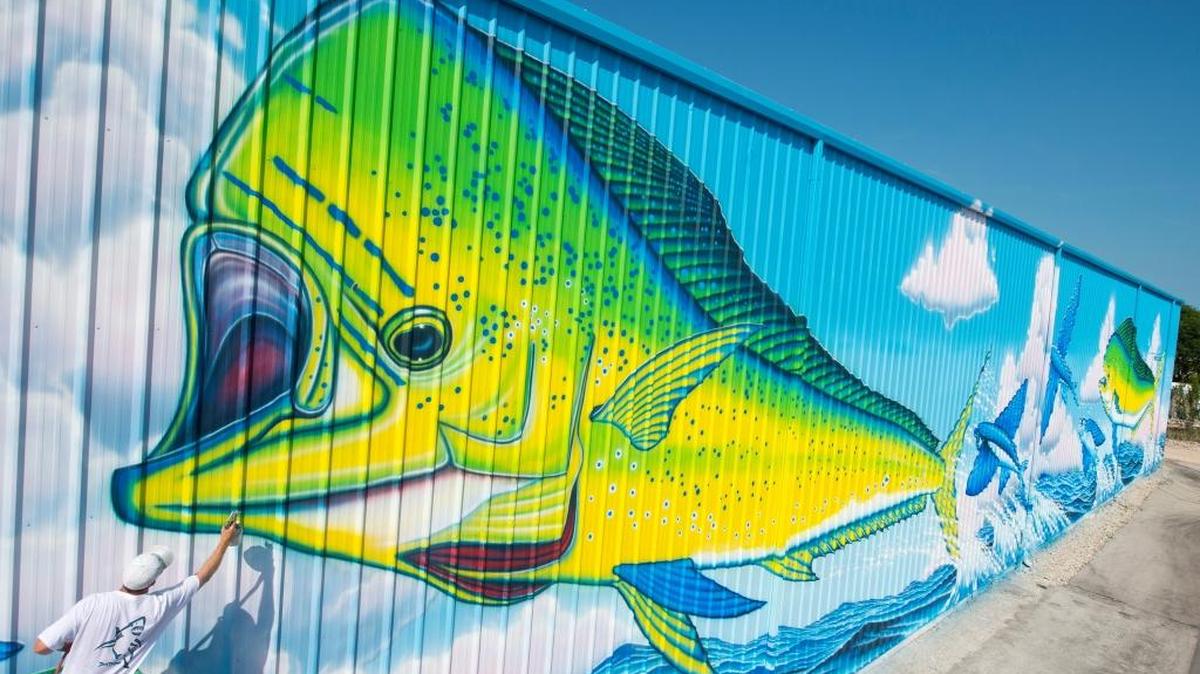 In this photo provided by the Florida Keys News Bureau, artist David Dunleavy, puts finishing touches on a huge mural entitled "Dolphin Rodeo" at an Islamorada, Fla., marina. The 252-foot-wide by 33-foot-high artwork features two dolphin, also known as mahi-mahi, that are popular ocean gamefish caught off the Florida Keys and other regions of the world. It took the New Jersey artist a month to paint his 62nd larger-than-life SeaLife Mural.