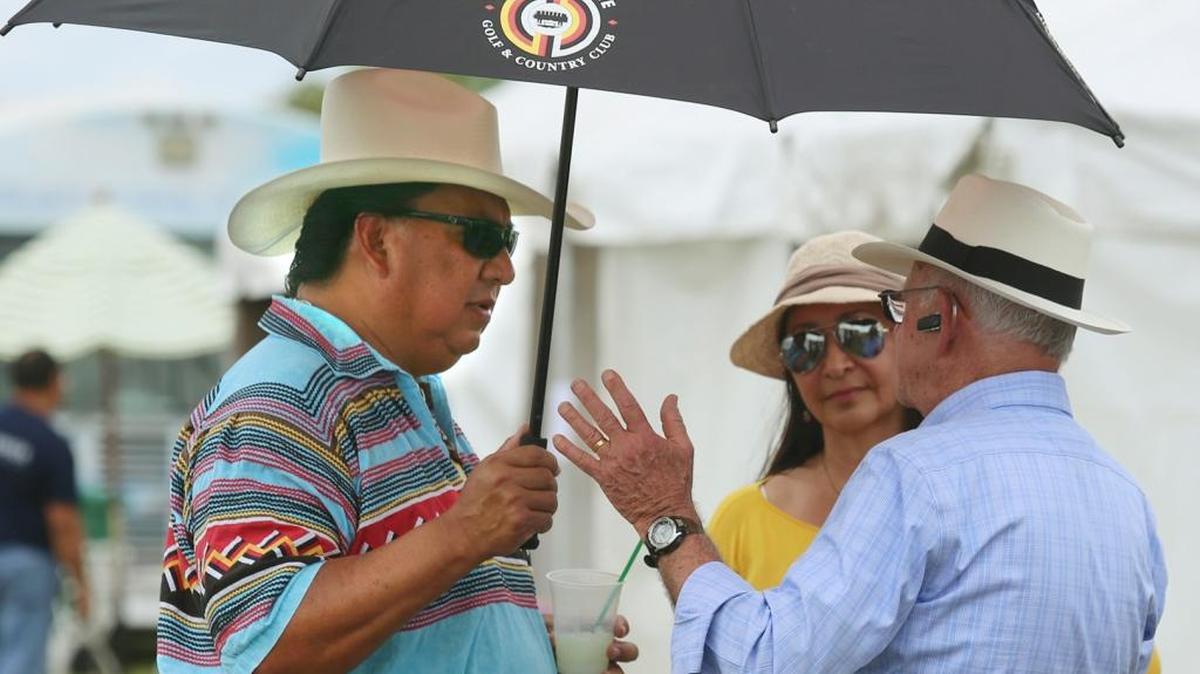 FILE--Colley Billie, chairman of the Miccosukee Tribe of Indians of Florida, left, talks with Miami Springs photographer Robert Holmes about how he created the "Gigapixel Panorama" photograph of downtown Miami at night, during the inaugural West End Art Fair on Saturday, April 18, 2015, in Miami's Kendall community. Billie and his wife, Consuelo Billie, second from left, were among hundreds of visitors to the inaugural West End Art Fair. The tribe’s general council voted Tuesday, Nov. 10, 2015, to remove Billie, who has two years remaining in his second term, as he attempted to settle the nasty legal battle with the Internal Revenue Service and started to withhold taxes from casino gambling distributions to some 600 members — a step the IRS demanded in legal action.