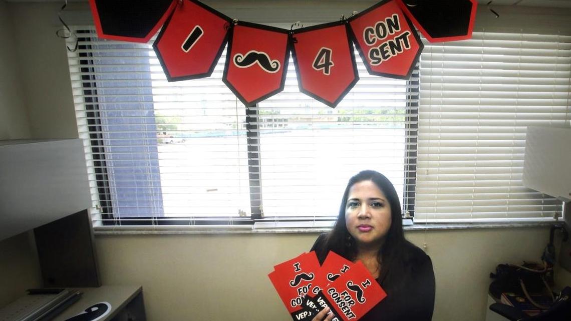 Wendy Ordóñez, outreach and educational media coordinator of Florida International University's Victim Empowerment Program, shows a banner and hand-out cards stating "I [Must Ask] 4 Consent," in her office at FIU's Sweetwater campus.