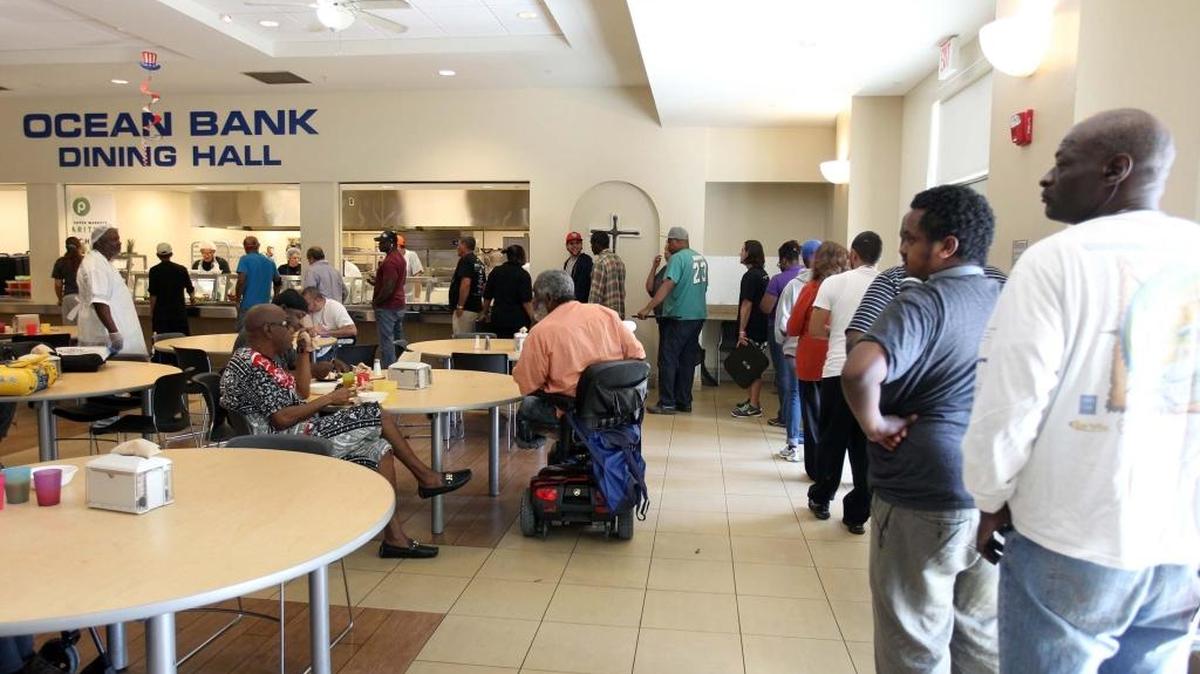 Persons wait in line to eat at the dining hall at Camillus House on Friday.