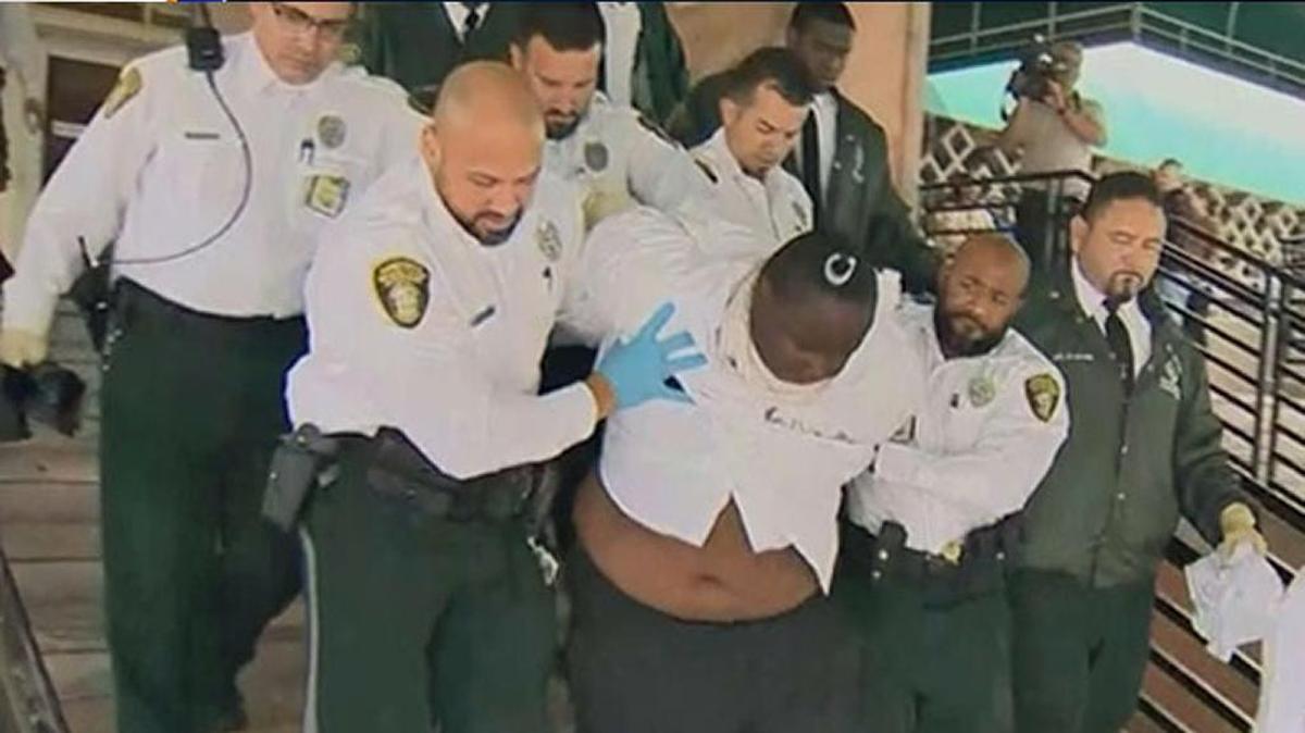 Godel Leveille is escorted to a police car by several officers after police say he bit a cop in a Miami-Dade courtroom.
