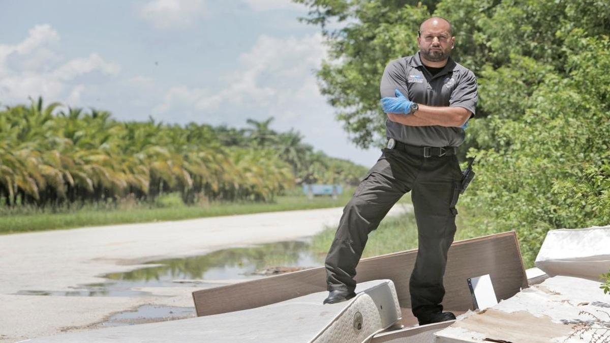 Santiago Callejas, an enforcement officer with Miami-Dade’s Solid Waste division, poses on a trash pile dumped illegally on a county road. A higher trash fee set to take effect Oct. 1 will boost the county’s enforcement actions against illegal dumping.
