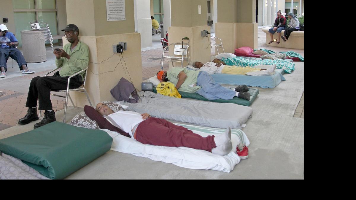 
Former Publix employee, Louis Michel, 62, left, sits back and checks his phone as others prepare their bedding for the night at Camillus House. The Overtown homeless shelter rolls out 115 mats for the homeless to sleep on, mostly outdoors beneath a pavilion on this May night. Photo taken Thursday, May 28, 2015.
