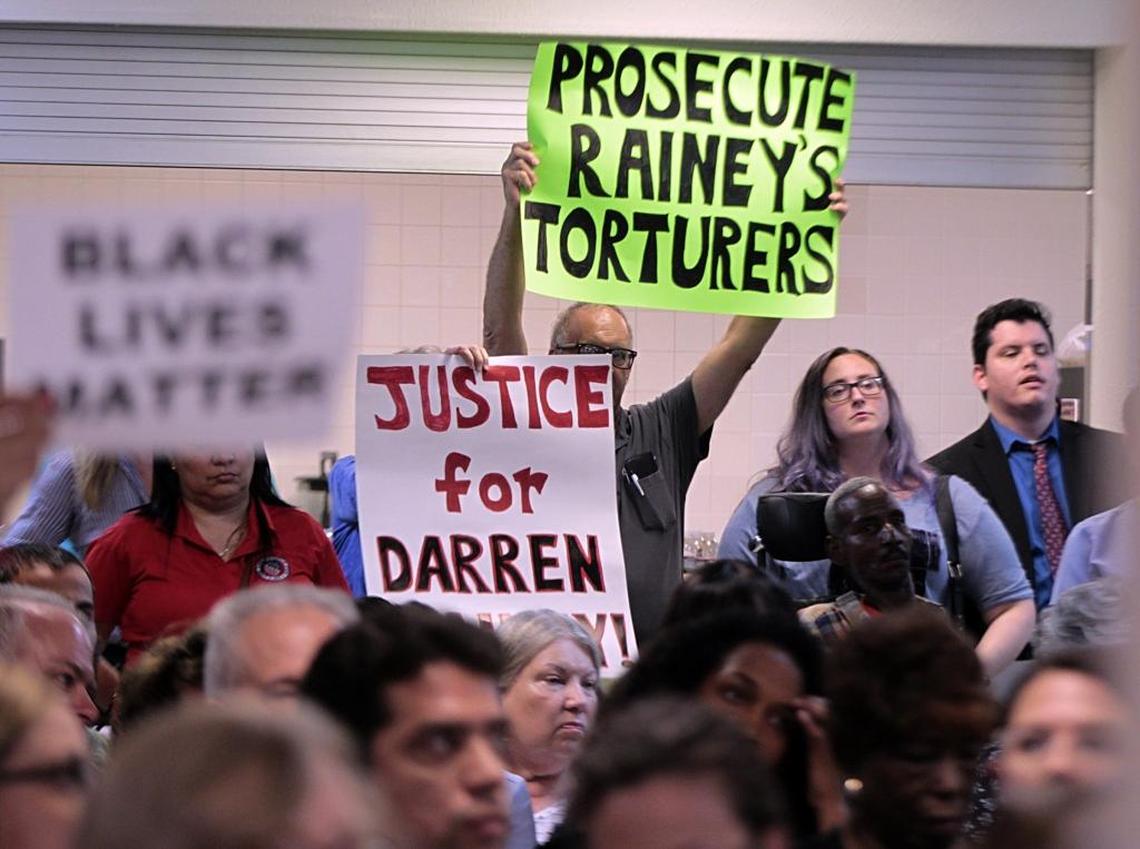 Protesters raise signs as State Attorney Katherine Fernandez Rundle speaks during a Miami-Dade Democratic Party meeting over her failure to mount a criminal case against the guards accused of putting inmate Darren Rainey in a searing shower. 