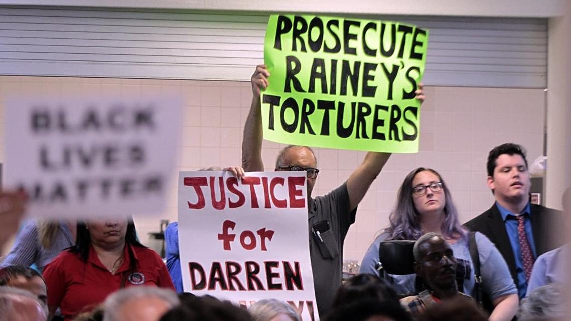Protesters raise signs as State Attorney Katherine Fernandez Rundle speaks during a Miami-Dade Democratic Party meeting over her failure to mount a criminal case against the guards accused of putting inmate Darren Rainey in a searing shower.