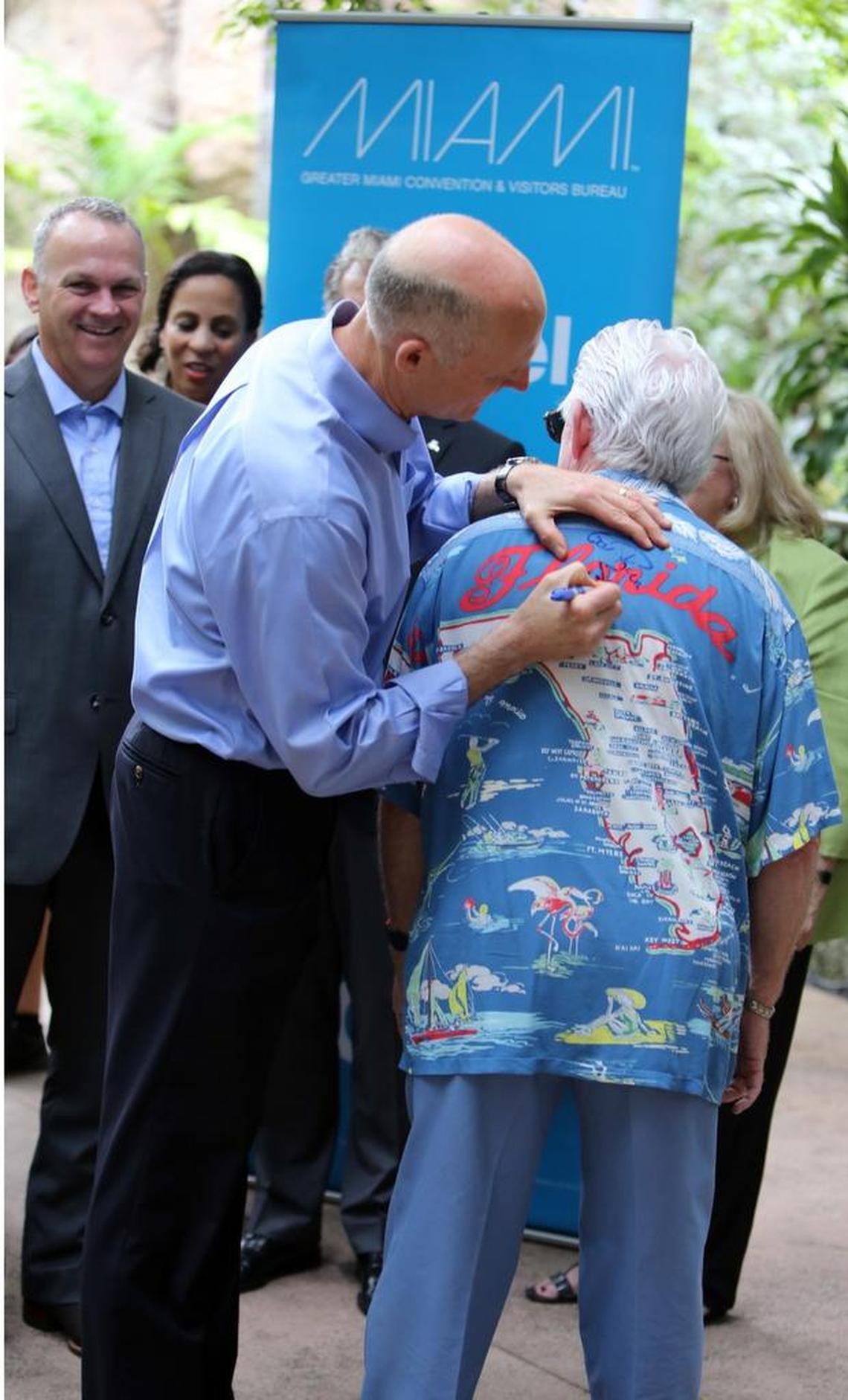 Governor Rick Scott signs the Florida shirt of William Talbert, president and CEO of the Greater Miami Convention & Visitors Bureau.