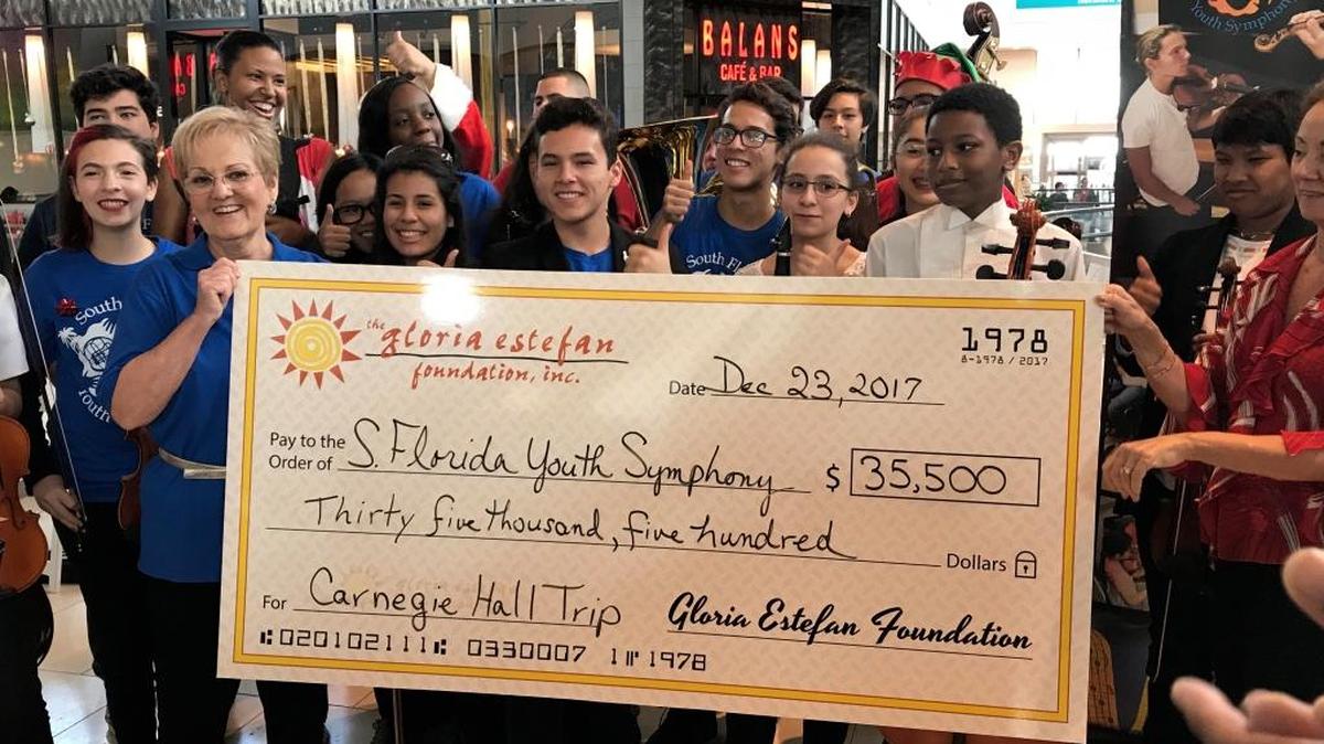 Marjorie Hahn, left, executive director of the South Florida Youth Symphony and symphony members are all smiles after receiving a donation for $35,500 from the Gloria Estefan Foundation. The donation will enable the award-winning orchestra to travel to New York City to perform at Carnegie Hall.