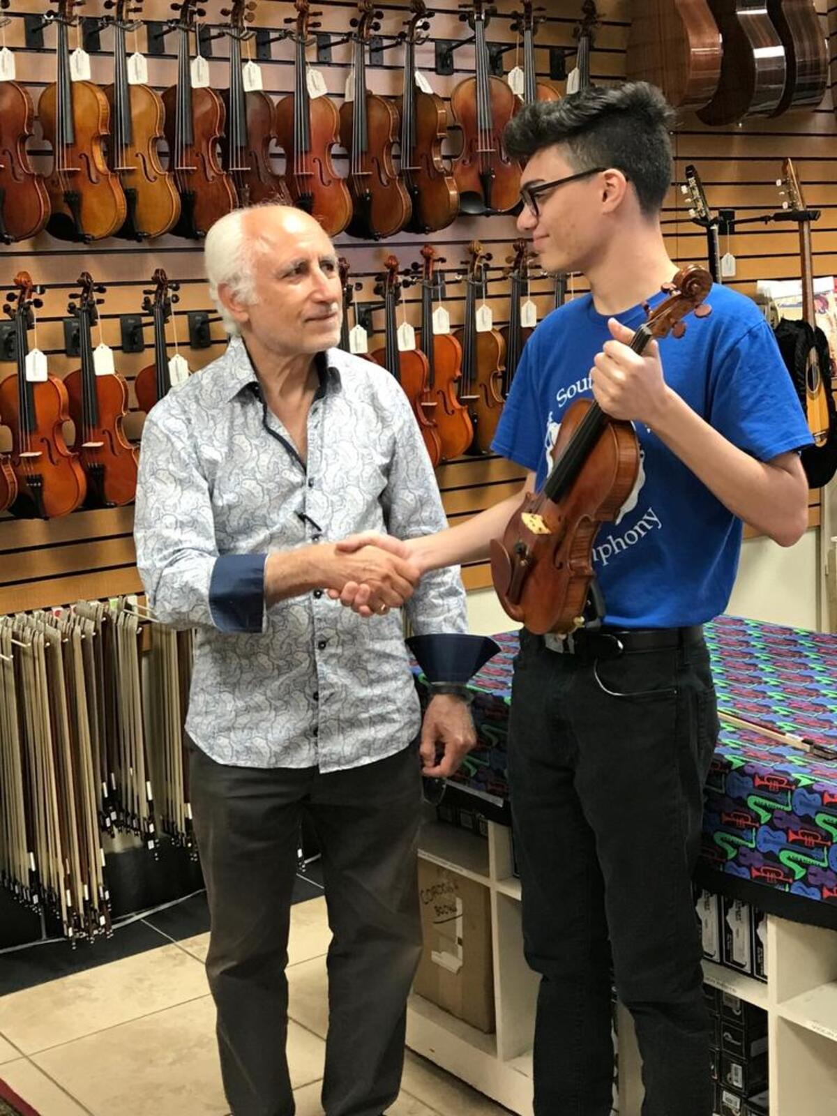 From left, Manuel Berberian, owner of Allegro Music Center in Miami, congratulates Yosvani Rodriguez, 16, on his scholarship to the Interlochen Center for the Arts.