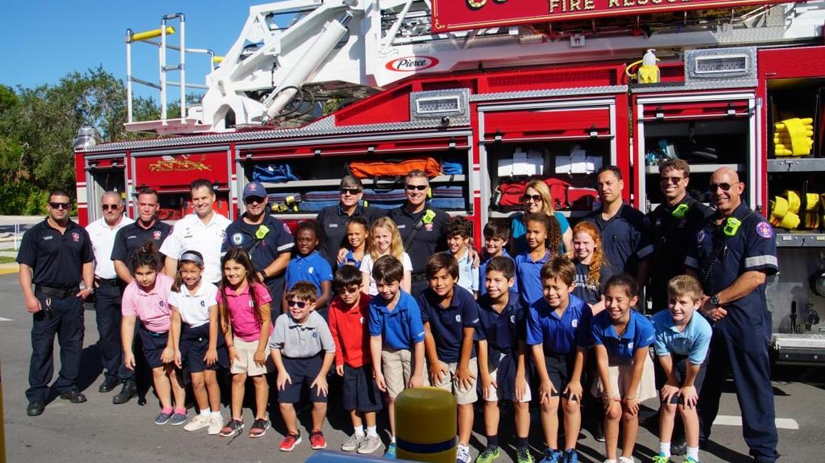 Some of Gulliver Schools’ third graders and their teacher welcome Coral Gables Fire Department fire rescue teams at a successful canned food drive for the Grove Outreach food bank.