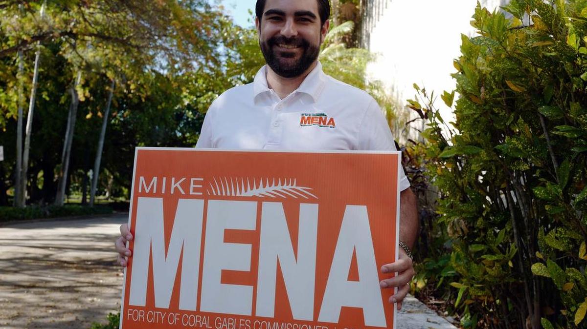 Attorney Michael Mena, holding his campaign sign outside the Coral Gables Library Tuesday. Mena won Tuesday’s runoff election for the Group 5 commission seat.