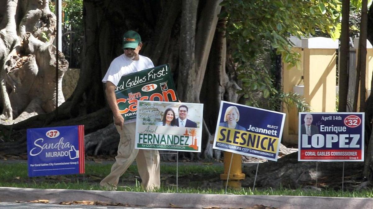 A supporter of Mayor Jim Cason sets a campaign poster next to the other candidates outside of the Coral Gables Congregational Church during the 2015 election. The city is considering charter changes including the creation of runoff elections.
