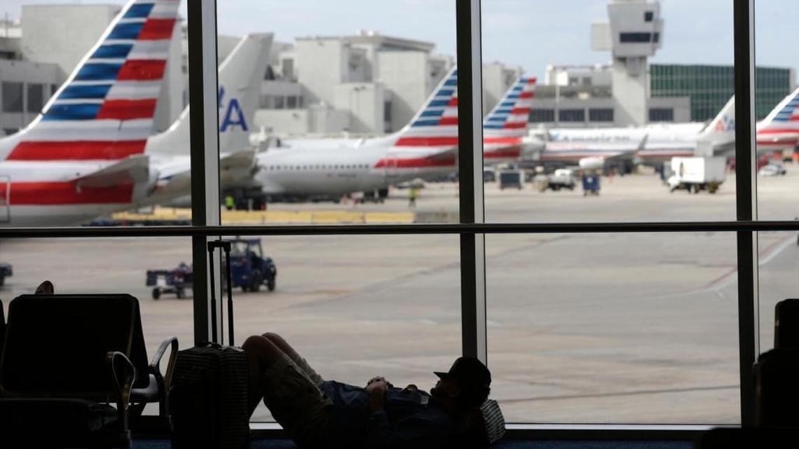 File photo: A traveler rests on the floor as American Airlines aircraft are lined up at the gates at Miami International Airport.