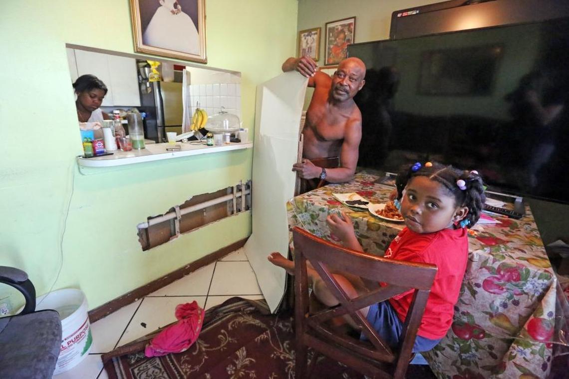 Luis David, 54, flanked by daughter Teslyn, 14, left, and granddaughter Elsa Miranda, 5, pulls back a piece of cardboard to reveal a large hole in his family’s living room wall. David has another hole in his kitchen closet ceiling.
