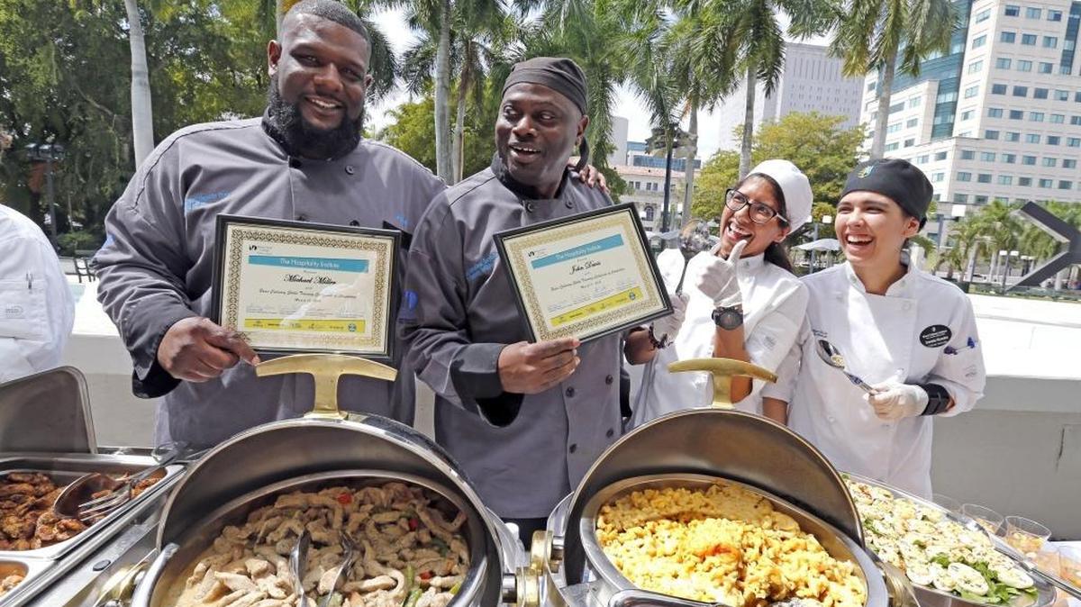 Michael Miller and John West Davis hold their diplomas after graduating ceremonies as Karina Ramo and Daniela Vicentini give them the thumbs-up at the after party, March 11, 2016. Miller and West have been residing at the Camillus House and have been taking culinary classes at Miami Dade College’s Hospitality Institute. Both men graduated Friday from the Wolfson Campus with a certificate in basic culinary skills training, and to top it off, Mr. Davis just landed a job at the University of Miami Hospital.