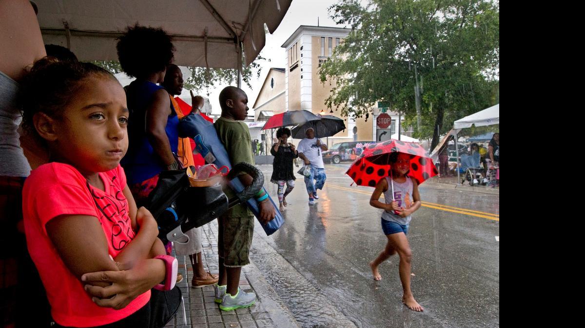 
Ariana DeFazio, 7, seeks shelter under a tent as it pours down rain at 9th street North West 3rd avenue during the 5th annual Overtown Music & Arts Festival on Saturday, July 25, 2015.
