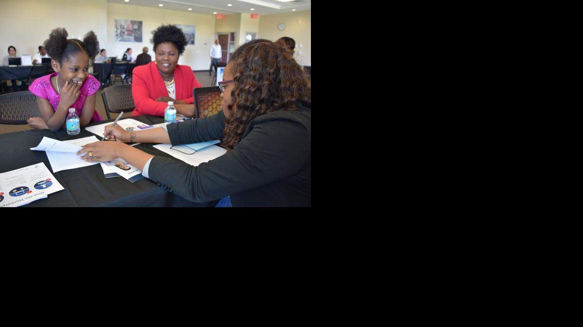 
Counselor with healthcare IT company Cognosante, Doulyne Seide, draws math problems for 7-year-old Alexandra Paul while she helps Alexandra’s mother, Merlene Paul (red blazer) sign up for healthcare coverage under the Affordable Care Act on Sunday at the Joe Celestin Community Center, 1525 NW 135th St., North Miami. 
