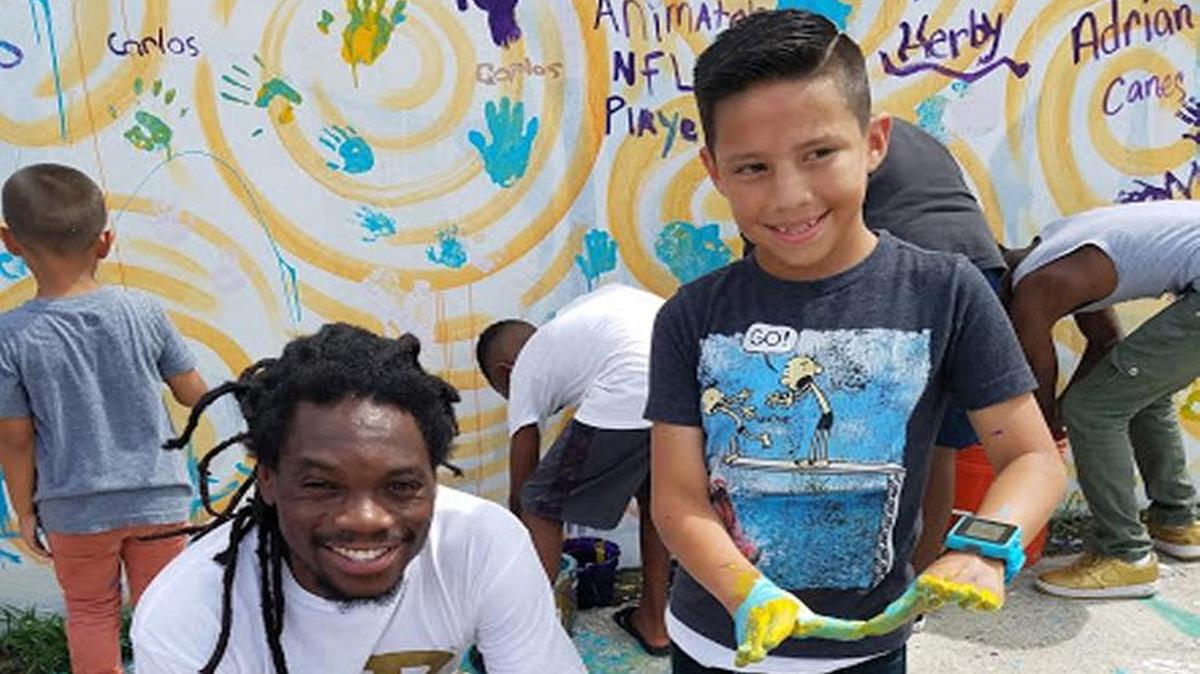 Miami rapper YD takes a break from helping to paint community mural to pose with a neighborhood child.