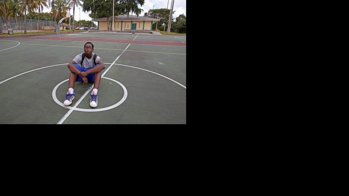 
Michael Dunconson, 16, sits on the basketball court at 8700 N.W. 17th Ave. on Tuesday, where 9 people were shot a day earlier. Michael said, "God helped me dodge a bullet" yesterday as he was going to meet two of his friends at the court to play basketball, but his bike was broken. He arrived at the park today looking for his friends and found out they were in the hospital.
