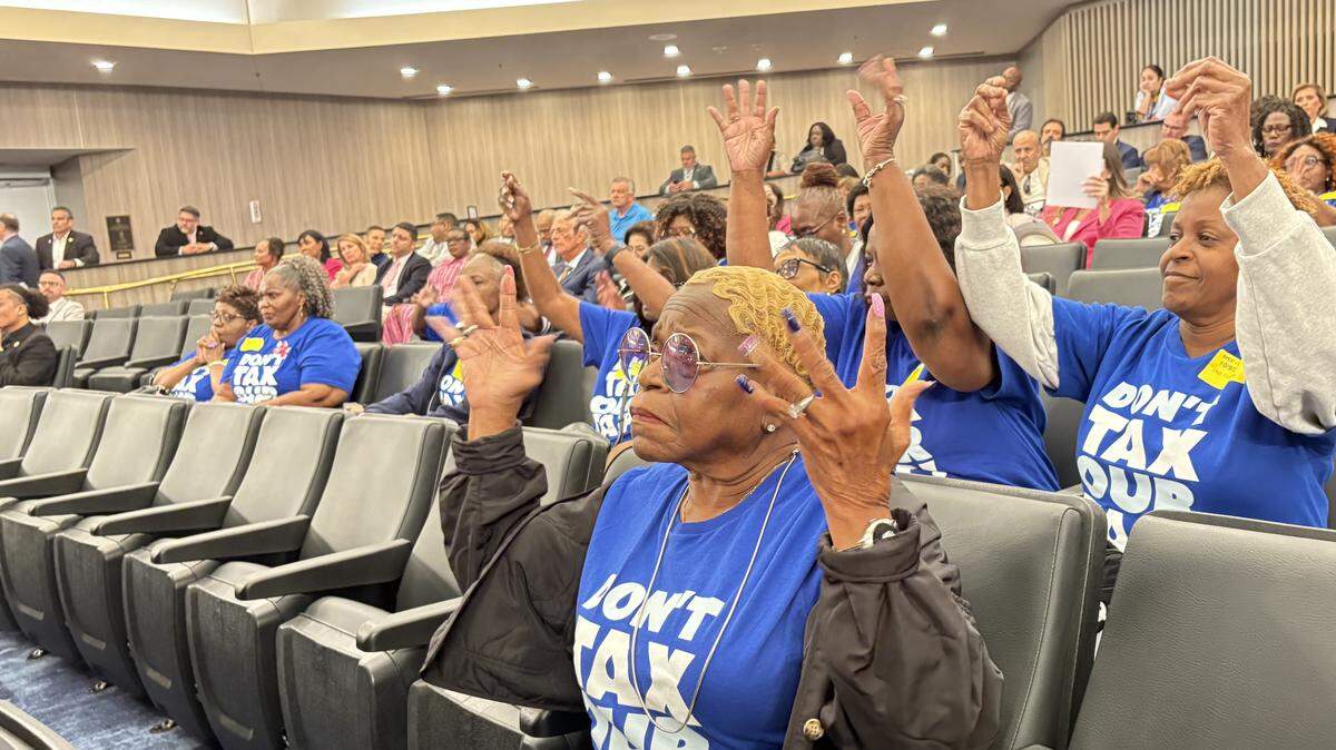 Constance Taylor, a Miami Gardens resident, raises her hands in support of Miami-Dade County legislation targeting a surcharge she pays for receiving water service from North Miami Beach. She joined other Miami Gardens residents in blue “Don’t Tax our Tap” T-shirts for the County Commission meeting on Thursday, Oct. 9, 2025.